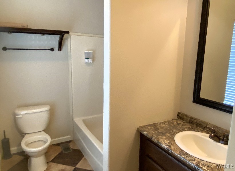 A small bathroom with a toilet, a bathtub-shower combo, a granite sink counter, and a mirror. Neutral tones create a clean, modern feel.
