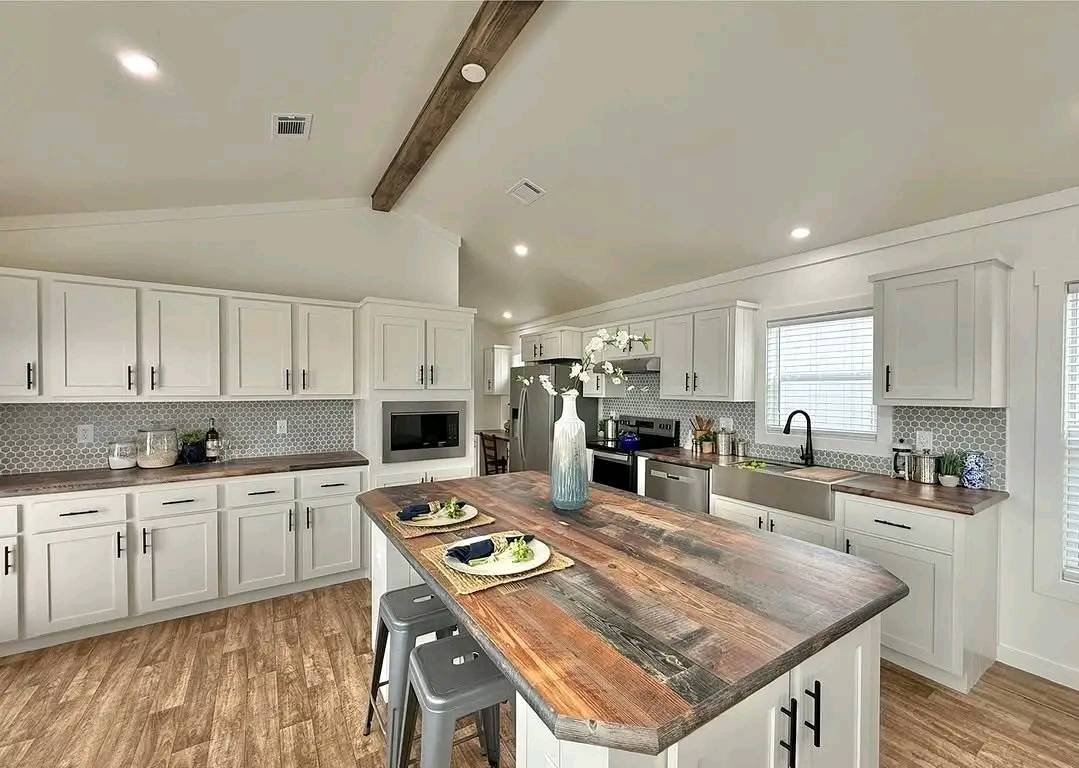 Modern kitchen with white cabinets, wooden countertops, and a large center island. It features bar stools, stainless appliances, and soft lighting for a cozy feel.