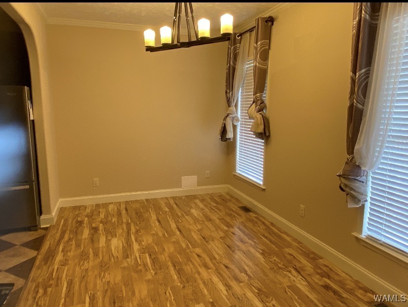 Empty dining room with light hardwood floors, beige walls, two windows with patterned curtains. A modern chandelier hangs from the ceiling. Quiet ambiance.