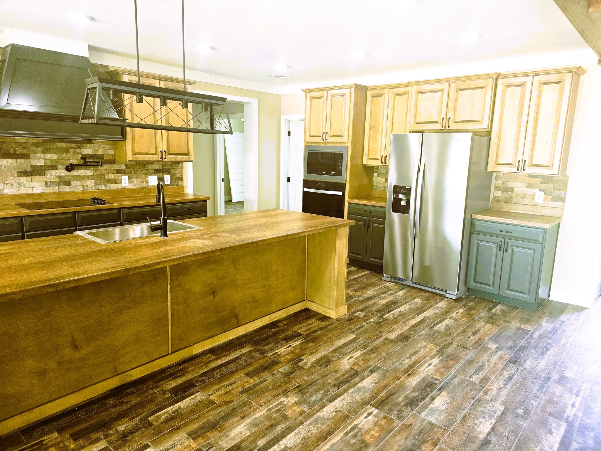 Spacious kitchen with rustic wood flooring, large island, dual sinks, and stainless steel appliances. Warm tone cabinets and earthy ambiance.
