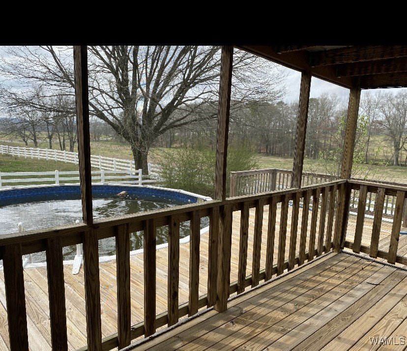 A wooden deck overlooks a round, partially filled outdoor pool with a backdrop of bare trees and a white fence. The scene is calm and rural.
