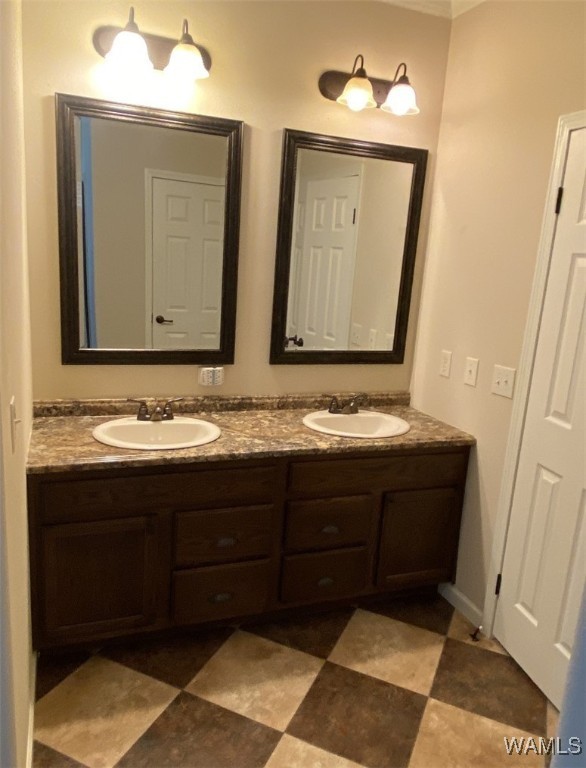 Dual-sink bathroom vanity with dark wood cabinets, granite countertop, and two mirrors. Overhead, warm-toned lights create a cozy ambiance.