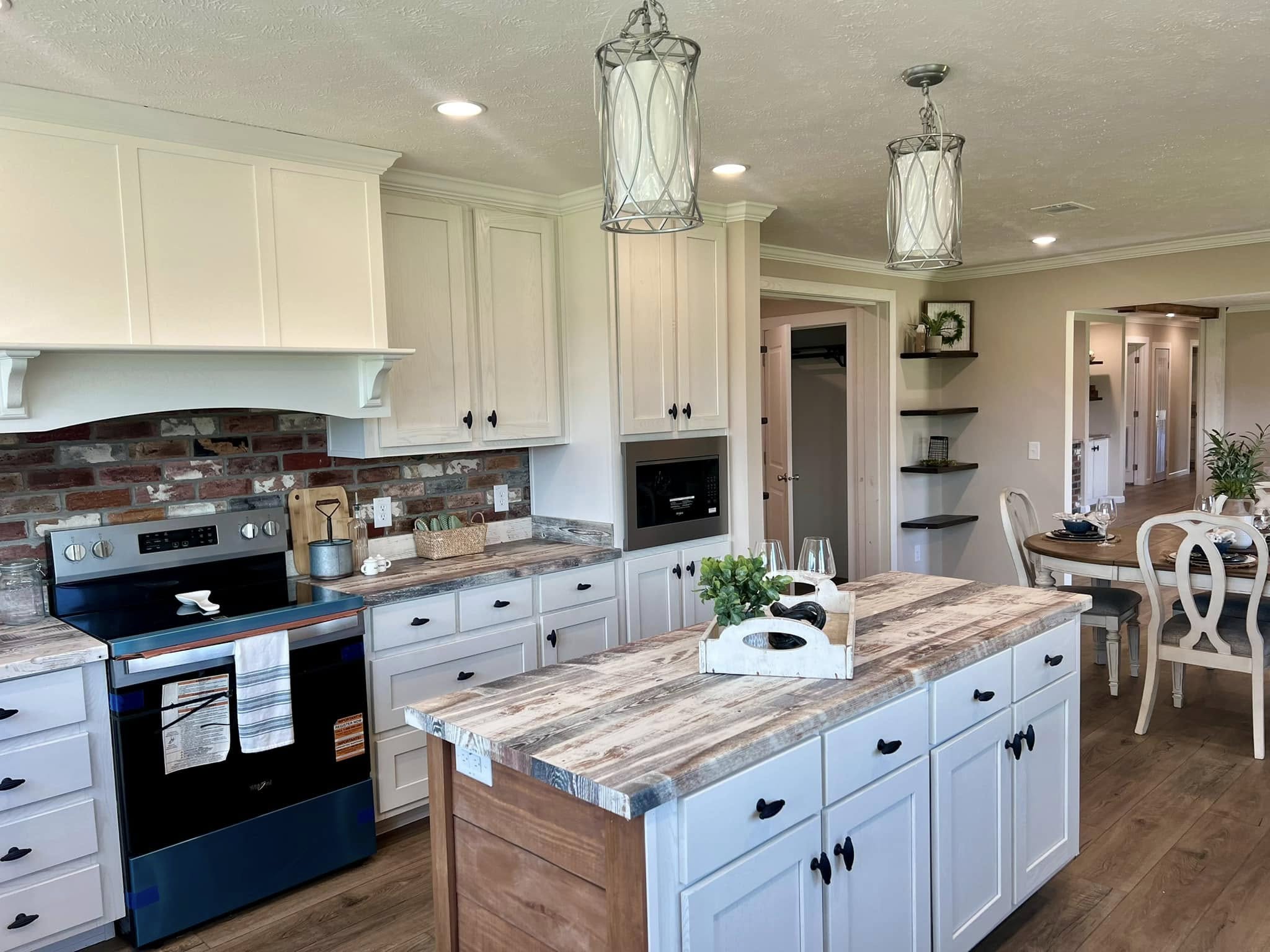 Spacious kitchen with rustic wood island, white cabinets, brick backsplash, and modern appliances. Pendant lights add a cozy ambiance.