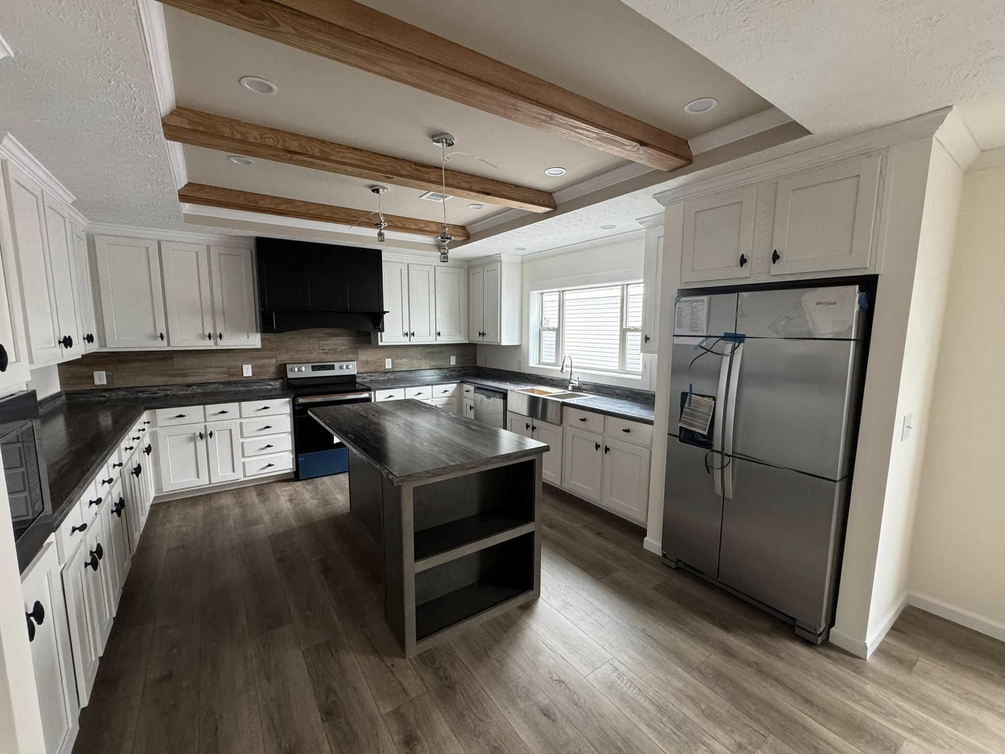 Spacious kitchen with white cabinets, dark countertops, and a stainless steel fridge. Wood beams and a dark island create a modern, cozy feel.