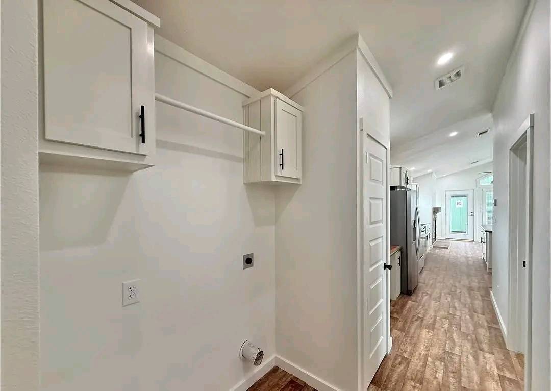 Bright laundry room with white cabinets and wood flooring, leading to a kitchen with stainless steel appliances. The space feels modern and airy.