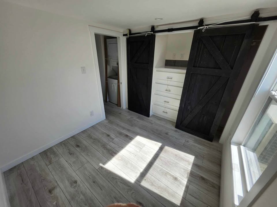 Sunny room with light wood flooring, featuring dark barn doors on a closet with white drawers inside. Bright and minimalistic ambiance.
