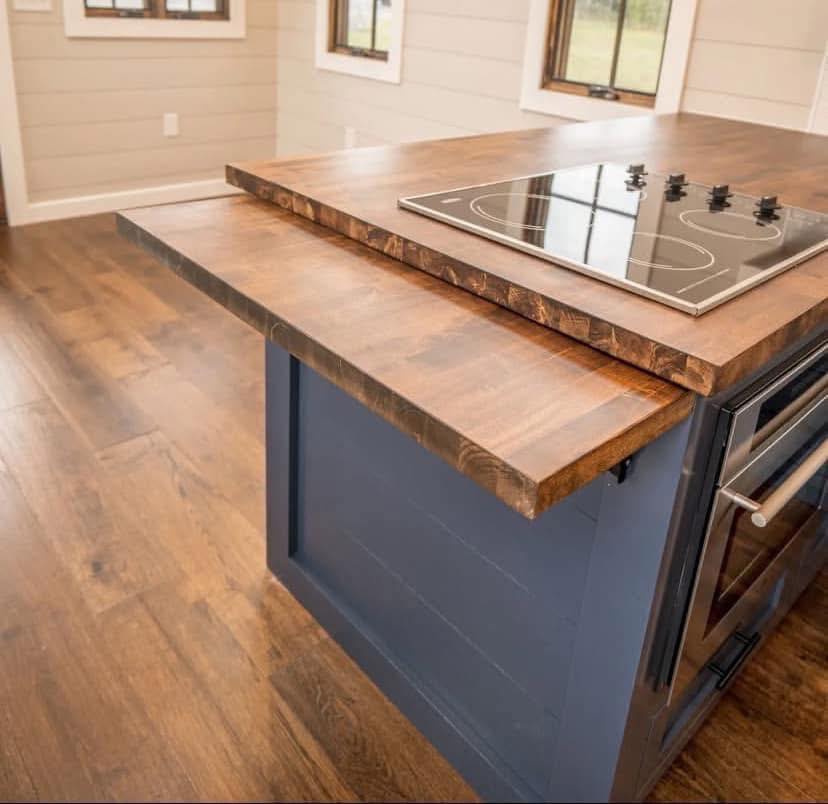 Modern kitchen island with a sleek wooden countertop and black electric stove. The warm, inviting space features wood panel walls and natural light.
