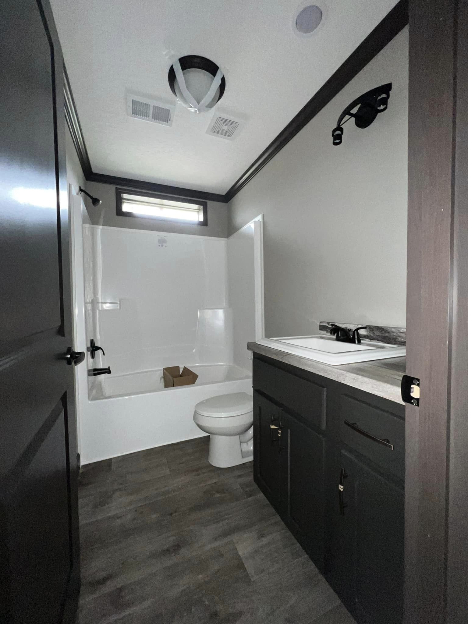 Modern bathroom with dark cabinets, white countertop, and a sleek sink. Light gray walls, dark wood floor, bathtub, and toilet in view. Minimalist design.