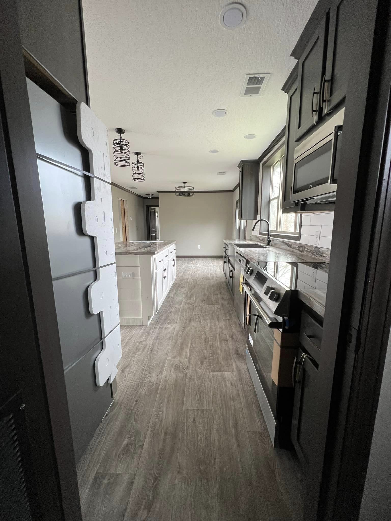 Modern kitchen with wooden floors, dark cabinets, and stainless steel appliances. Center island with pendant lights creates a sleek, inviting atmosphere.