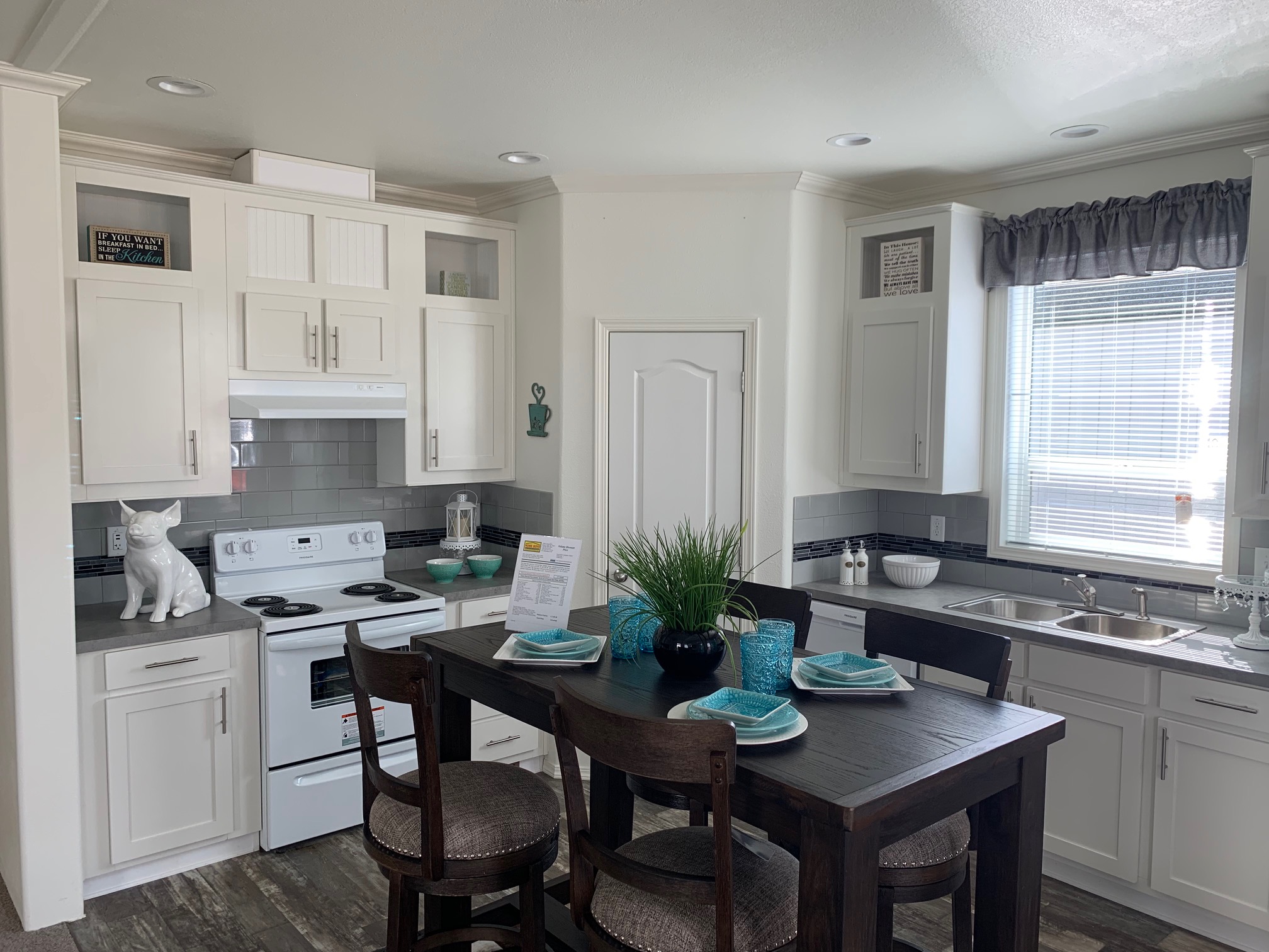 Bright kitchen with white cabinets, gray countertops, and a dining table set. Decorative items include a white dog sculpture and turquoise accents.