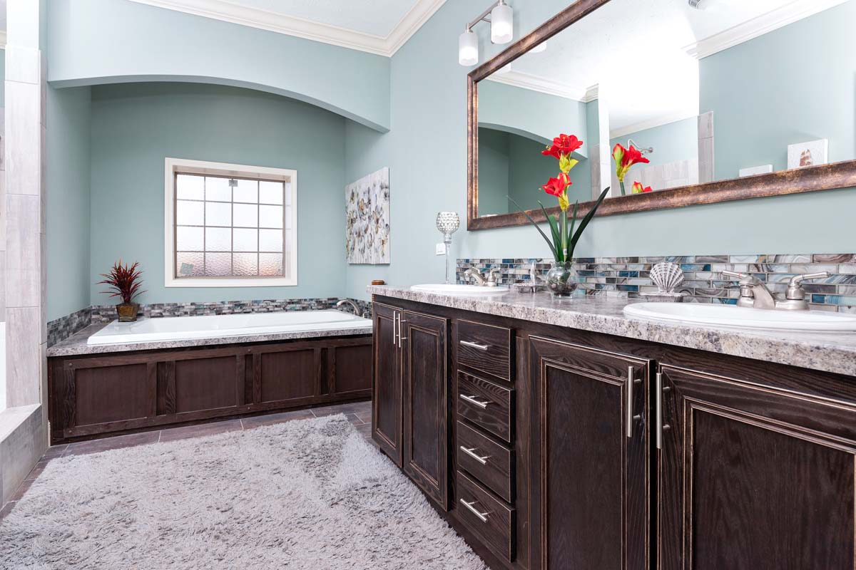 Luxurious bathroom with dark wood cabinets, marble countertops, and twin sinks. A large mirror, red flowers, and a tub add elegance to the serene space.