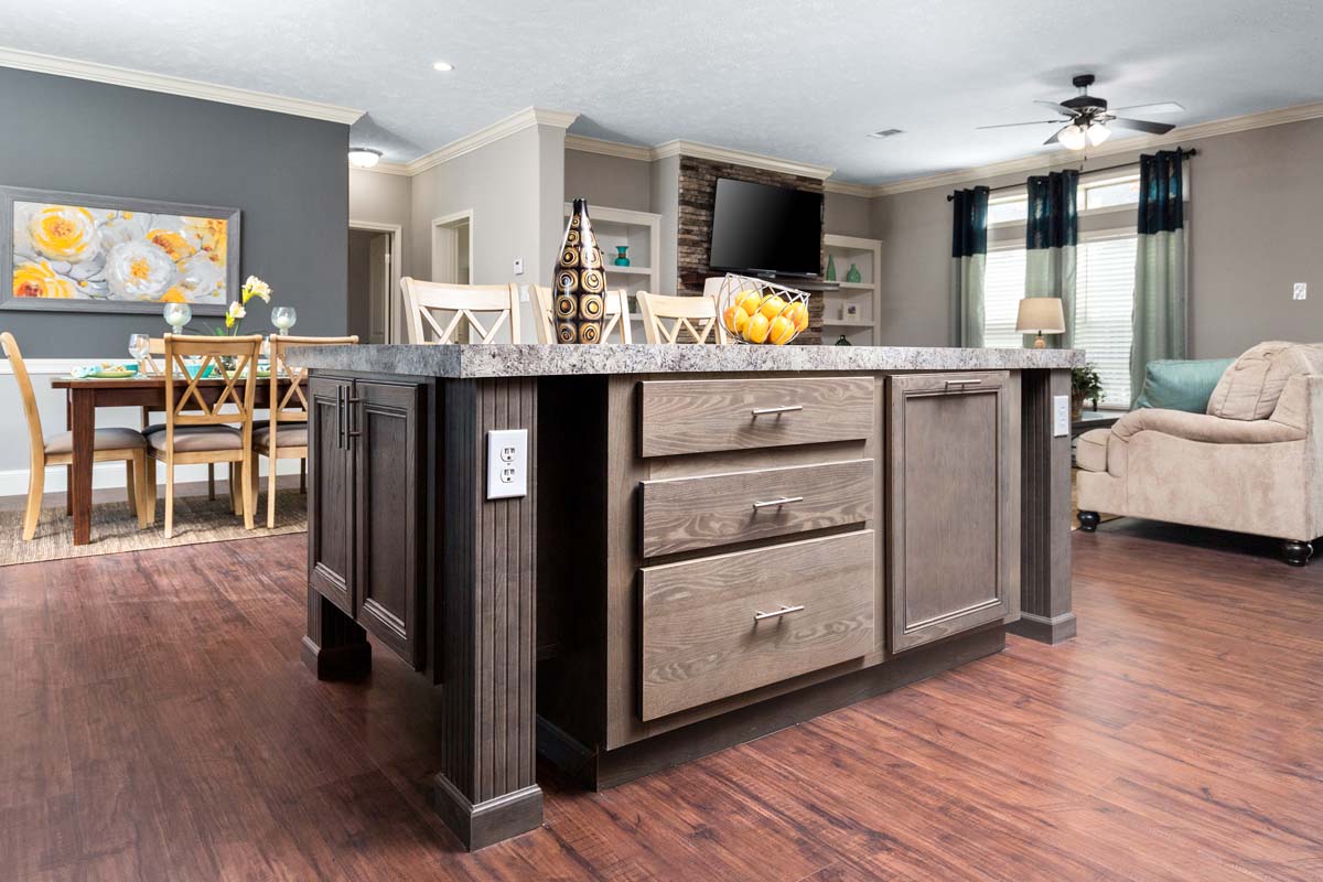 Spacious modern living area with hardwood floors, a large kitchen island, cozy beige sofa, dining table with floral centerpiece, and bright, airy decor.