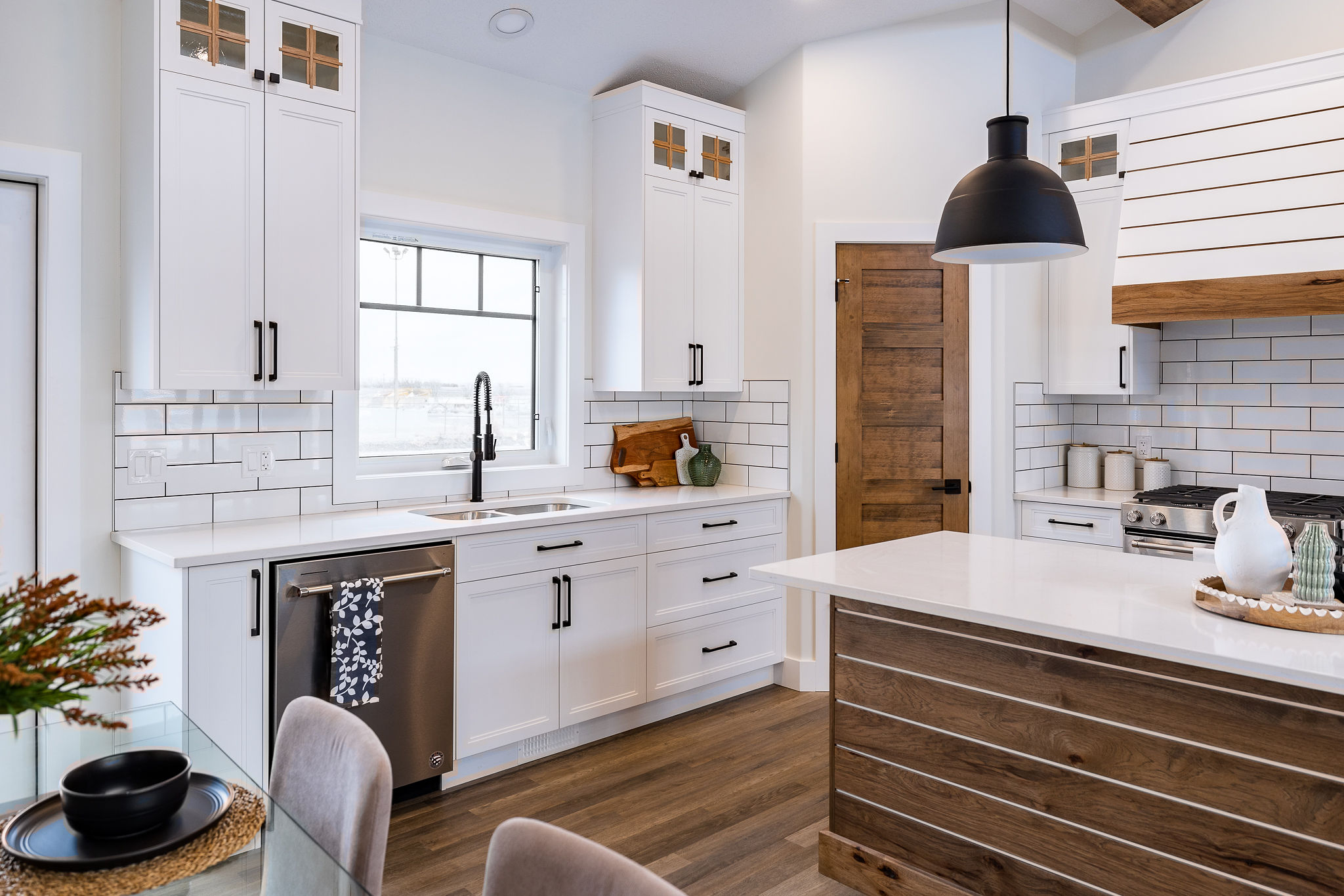 Modern kitchen with white cabinets, wood accents, and a subway tile backsplash. Features include a black pendant light, stainless steel appliances, and ceramic decor, creating a cozy, elegant atmosphere.