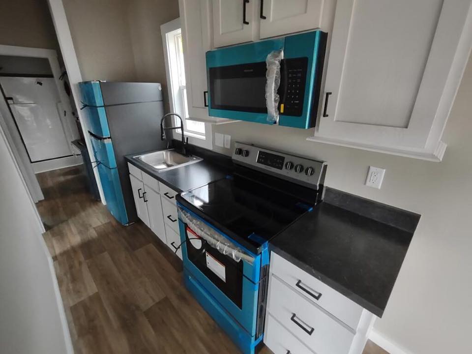 Modern kitchen with a sleek black countertop, blue appliances, and white cabinets. Features a stainless steel sink and wood-style flooring.