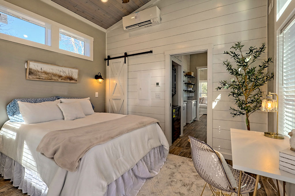 Cozy bedroom with a plush bed, rustic barn door, and a small desk. Soft lighting, an indoor plant, and neutral tones create a calm atmosphere.