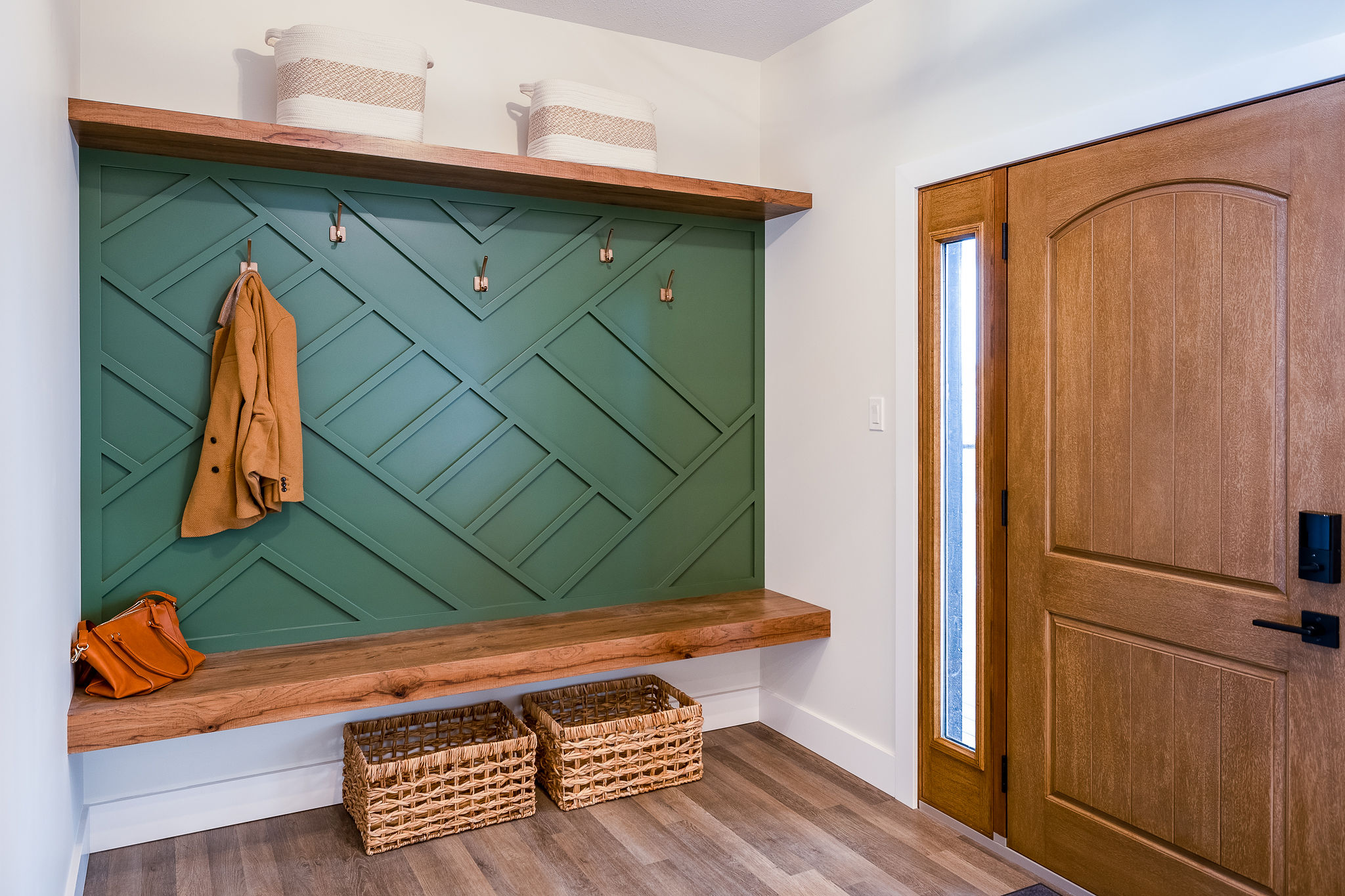 Entryway with a green accent wall featuring wooden hooks, a wooden bench, and two baskets below. A coat hangs on a hook, and a purse is on the bench.