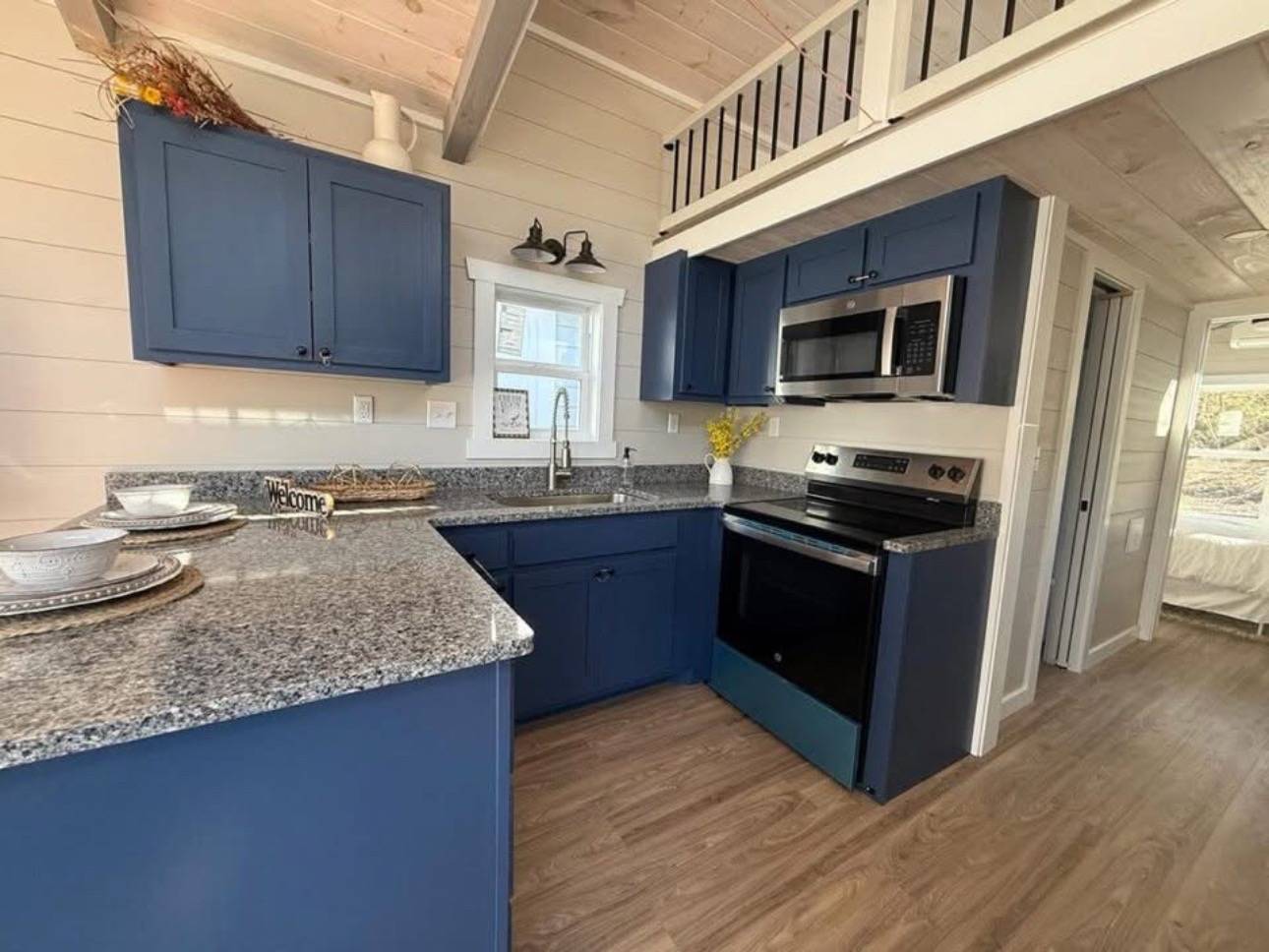 Stylish kitchen with blue cabinets, granite countertops, and stainless steel appliances. Loft with railing above, creating a cozy, modern ambiance.