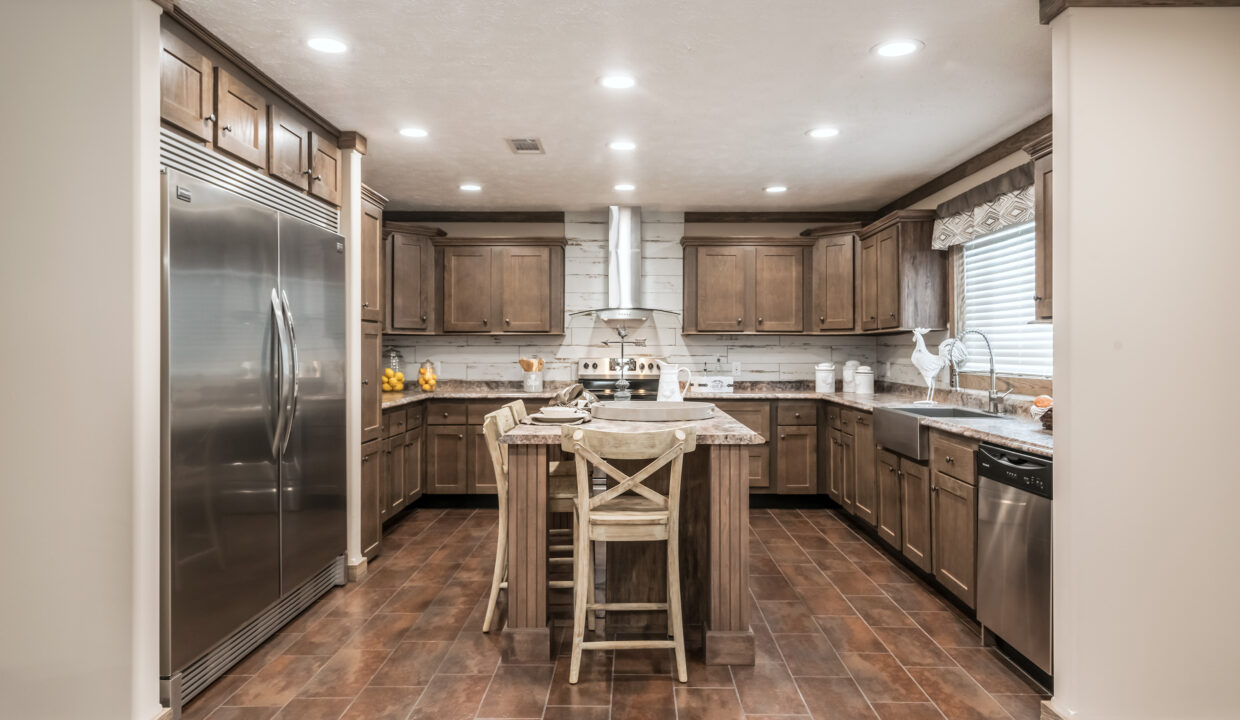 Spacious kitchen with wooden cabinets, a central island with two chairs, stainless steel appliances, recessed lights, and warm brown tones. Cozy ambiance.