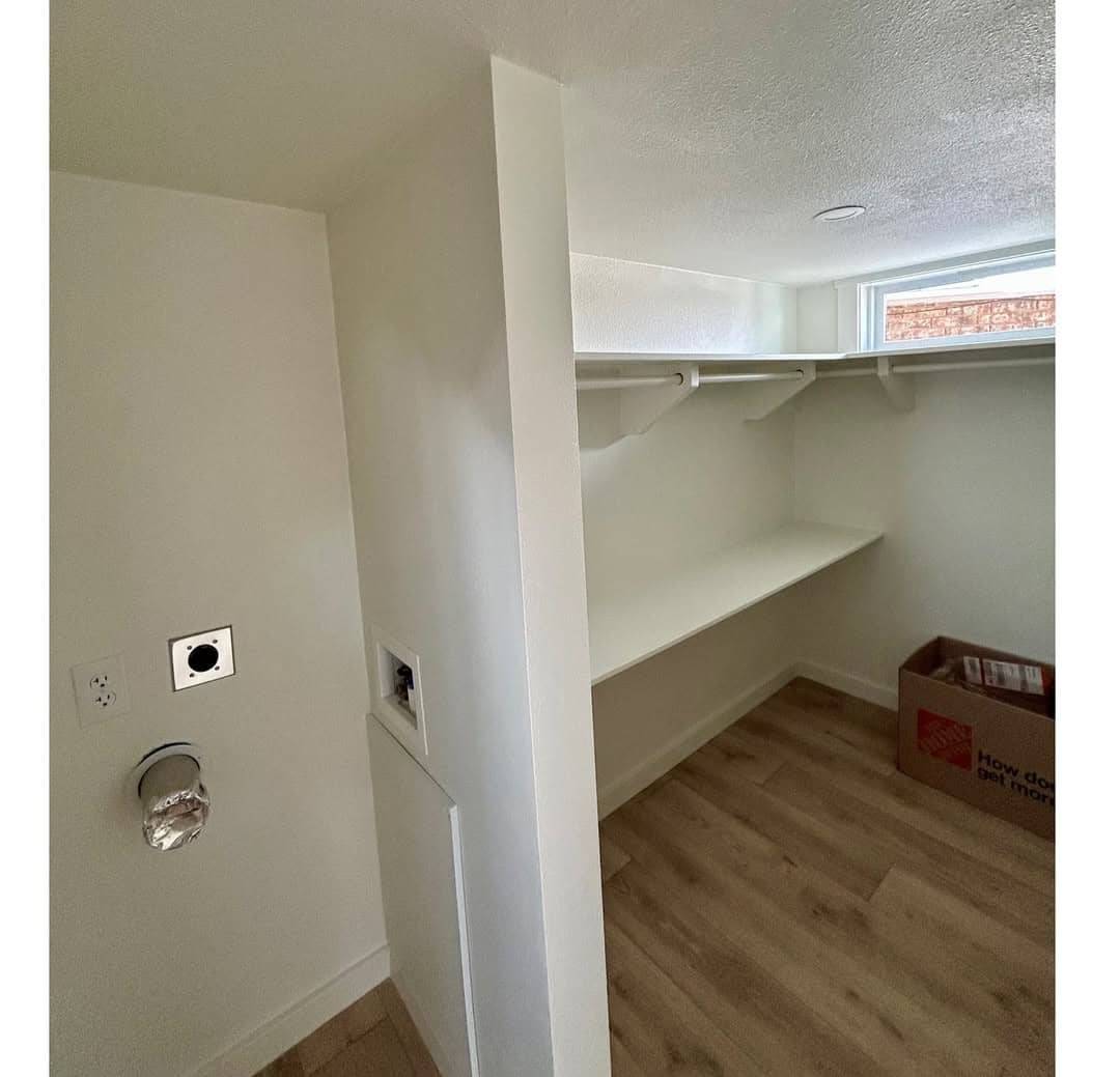 Empty white closet with light wood flooring, shelves, and a rod for hanging clothes. A wall has wrapped outlets, and a box sits on the floor. Bright, minimalistic.