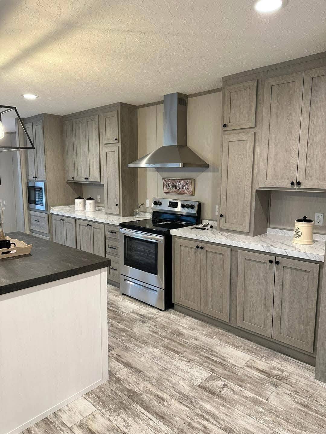 Modern kitchen with gray wood cabinets, stainless steel appliances, and marble countertops. Light wood flooring contrasts with dark accents, creating a sleek, inviting atmosphere.