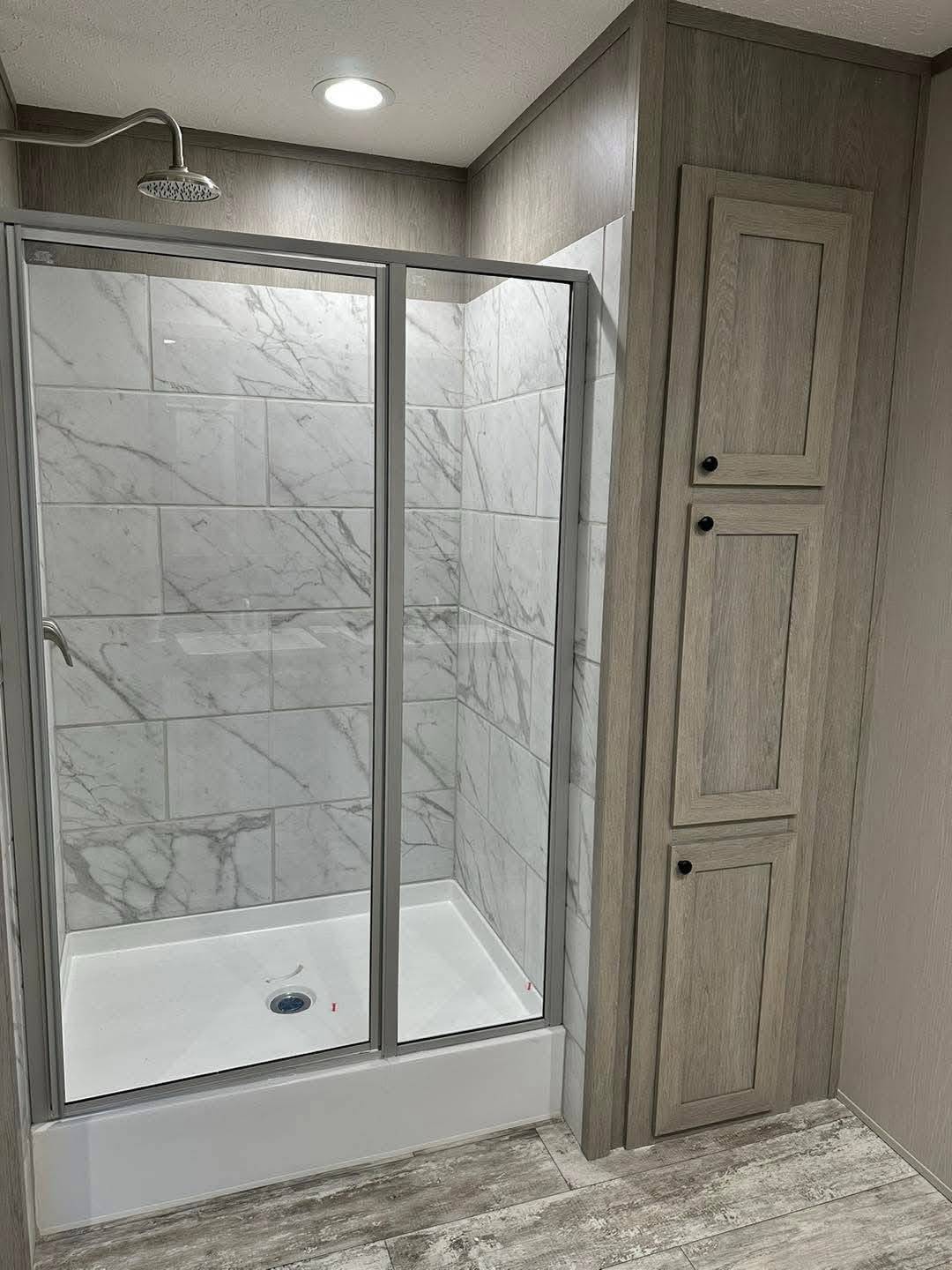 Modern bathroom with a marble-tiled shower and sliding glass doors. Adjacent light wood cabinets add a sleek, minimalist touch. Soft, natural lighting.
