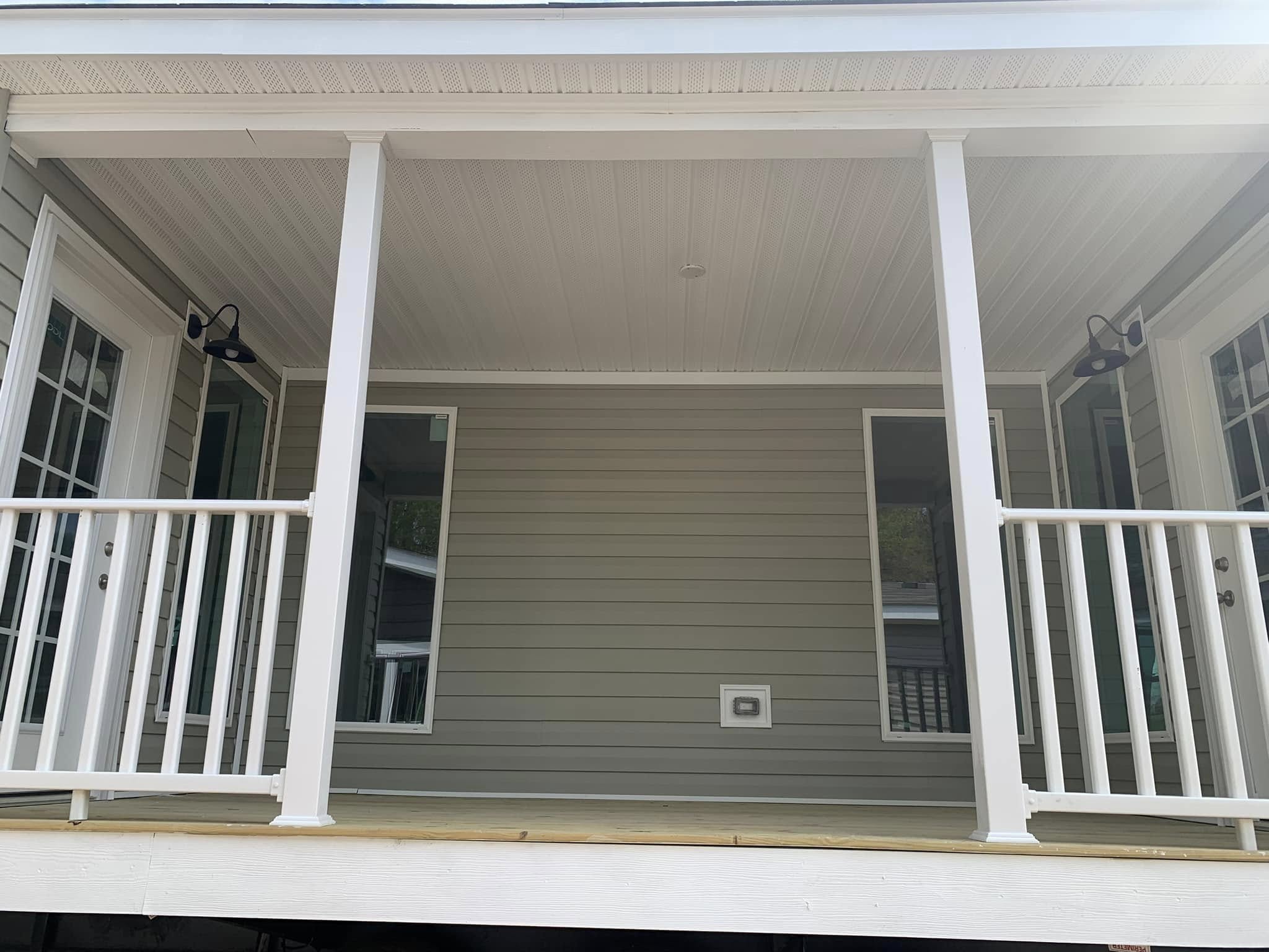 Front porch with white railings and gray siding, featuring two black lantern-style lights beside glass doors. The scene feels calm and inviting.