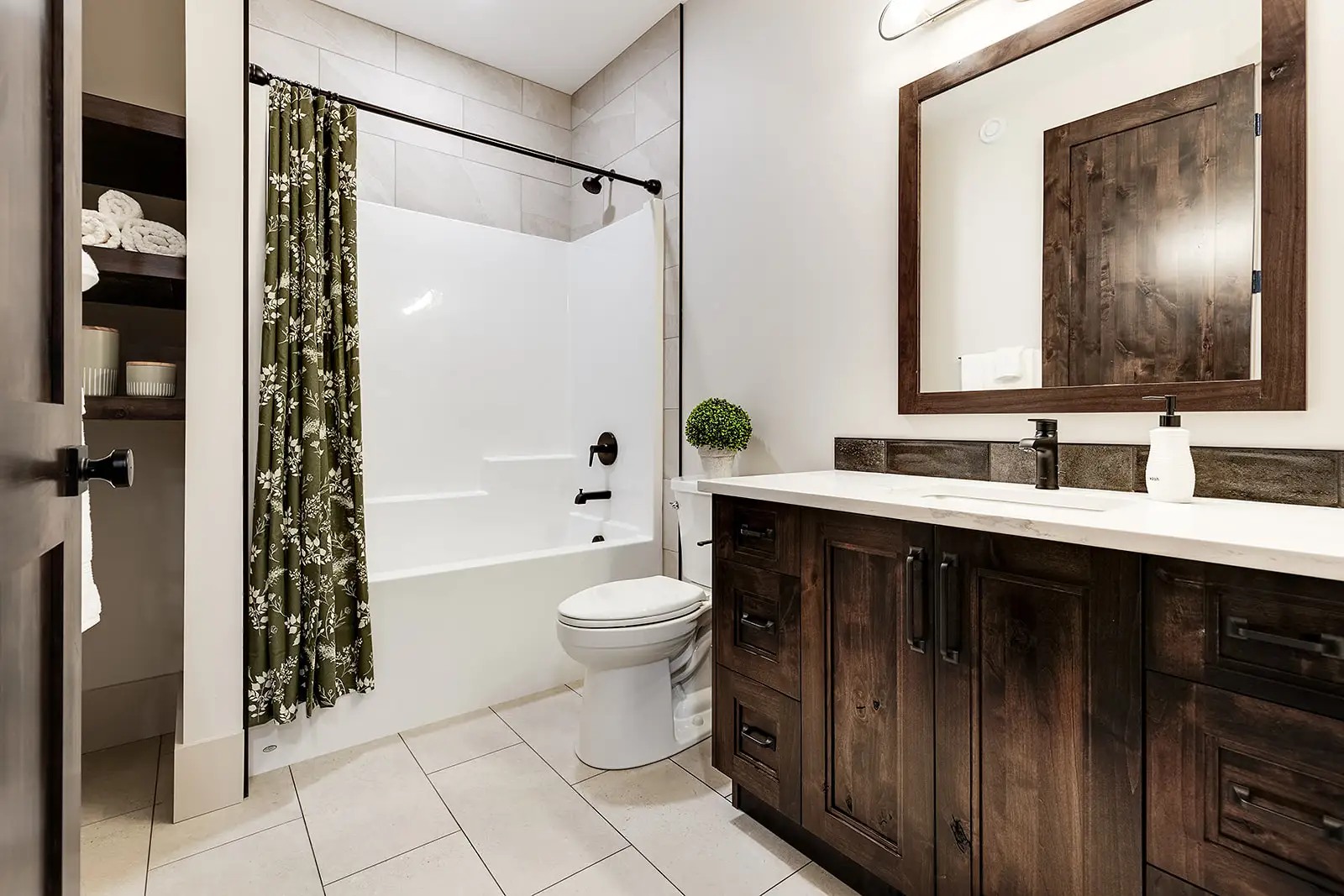 Modern bathroom with dark wood cabinets, large mirror, white bathtub, and toilet. Green floral shower curtain adds a touch of elegance.
