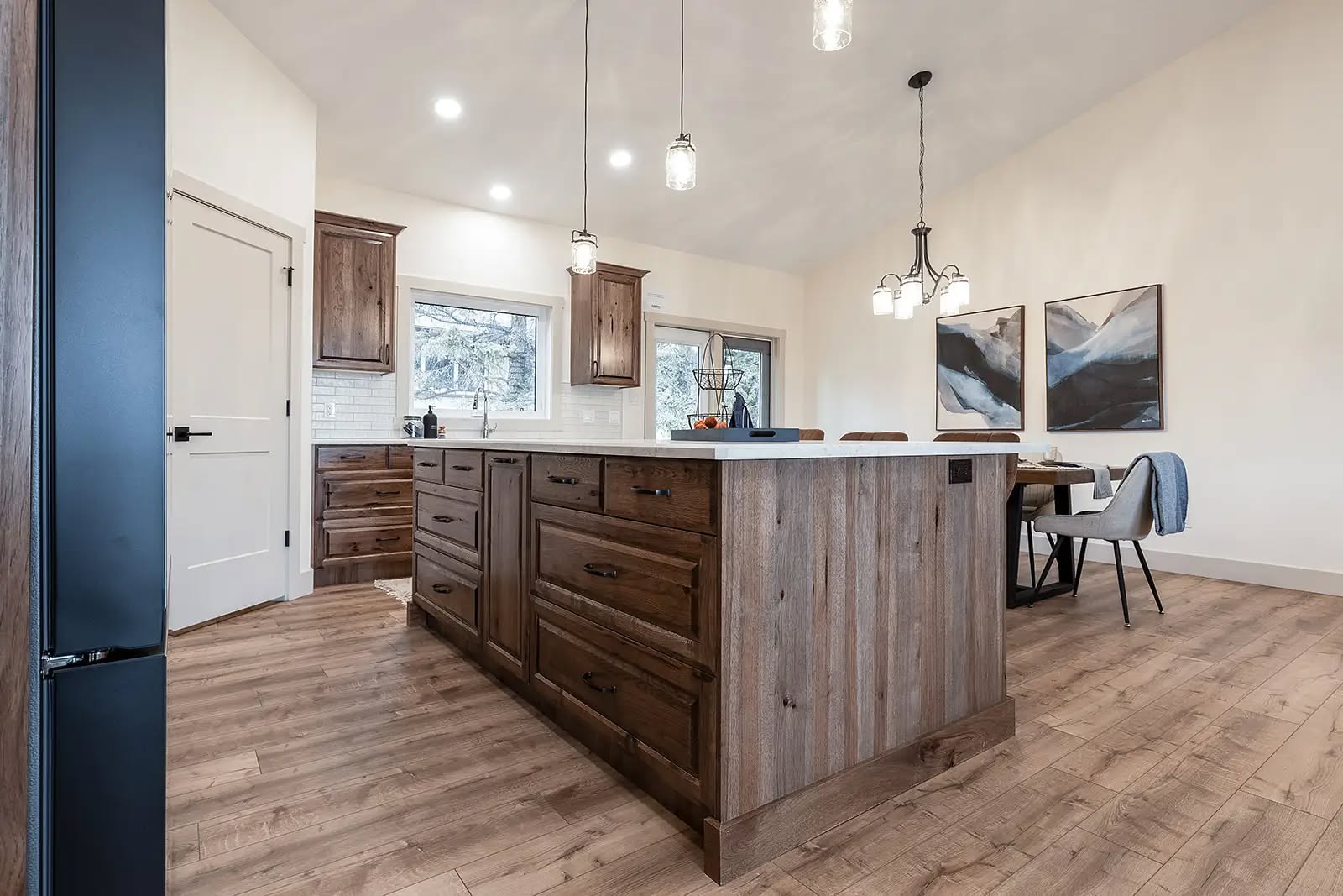 Spacious kitchen with rustic wood island, pendant lights, and modern decor. Light wood floors, artwork on walls, and natural lighting create a cozy atmosphere.