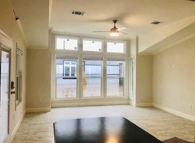 Spacious, neutral-toned living room with large windows and a ceiling fan. Sunlit, minimalist style with hardwood floors, creating a warm, inviting atmosphere.