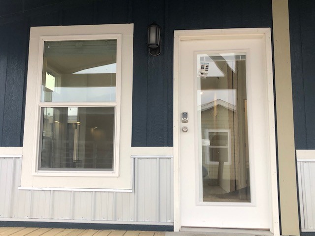 A blue exterior wall with a white-framed window and glass door. A black wall light is mounted above, conveying a clean and modern feel.