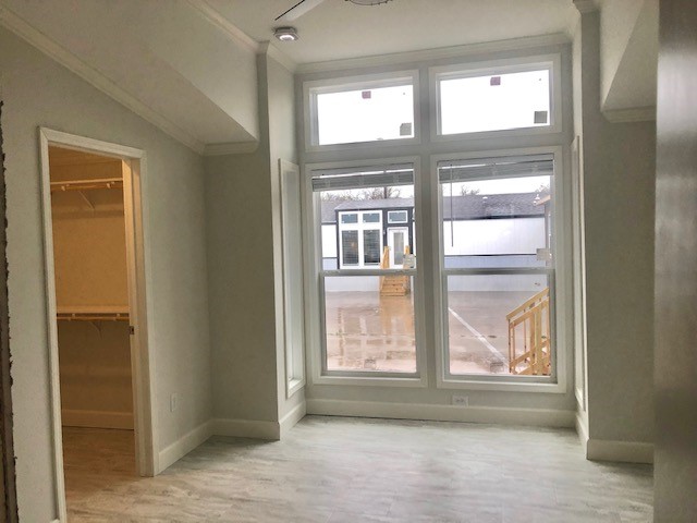Bright room with large floor-to-ceiling windows, light wood flooring, and an open doorway leading to a closet. Outdoors, a small building is visible.