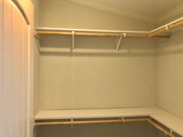 Empty walk-in closet with beige walls and wooden shelves. Clean and organized, conveying a sense of simplicity and potential for storage.