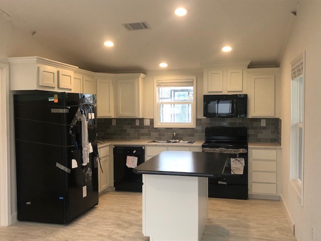 A modern kitchen with white cabinets, black appliances, and gray tile backsplash. Central island with overhead lights gives a fresh, clean feel.