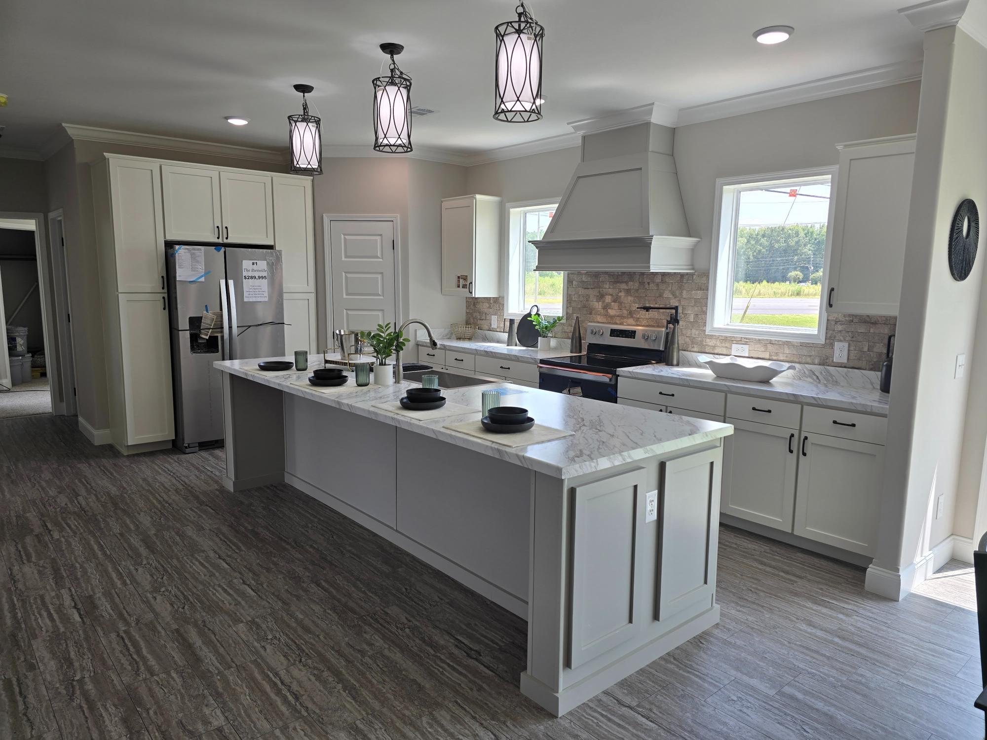 Modern kitchen with white cabinets, large island with marble countertops set for four, and three pendant lights. Bright, airy feel with natural light.