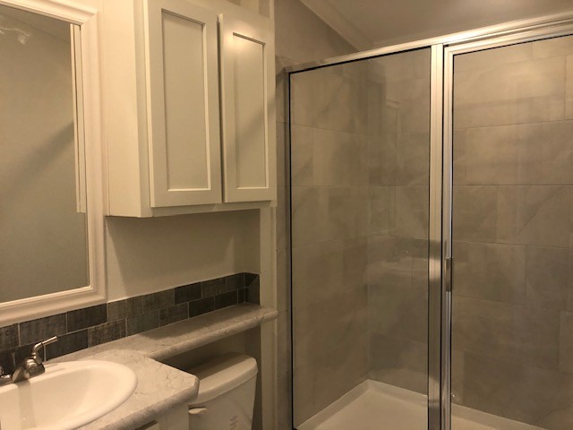 Modern bathroom with a large glass shower, light gray tiles, a white vanity with a marble countertop, and dark backsplash. Minimalist and clean design.