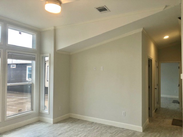Bright, modern room with a vaulted ceiling, large windows, and light-colored walls and floor. A hallway leads to multiple doors, creating an inviting, airy feel.