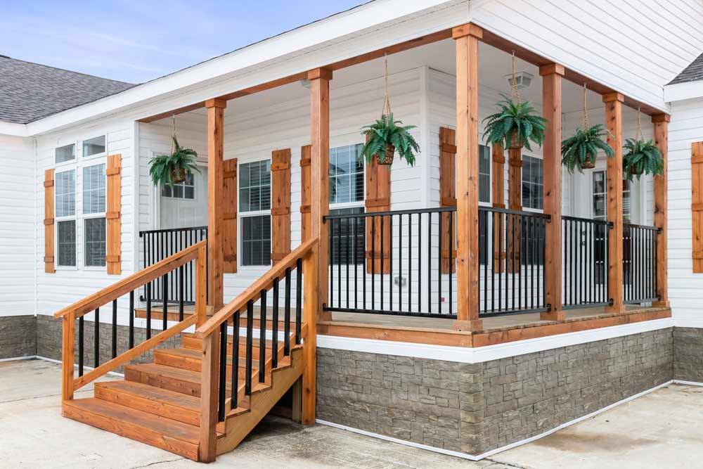 A cozy white porch with wooden pillars and black railings, adorned with hanging green ferns. Wooden shutters complement the inviting atmosphere.