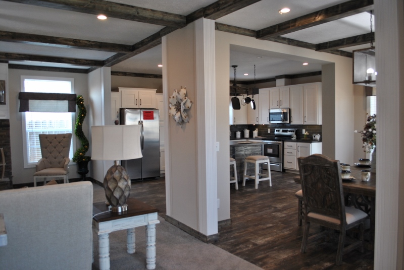 Spacious open-concept kitchen and dining area with rustic beams, white cabinets, stainless steel appliances, and dark wooden floors. Inviting and cozy.