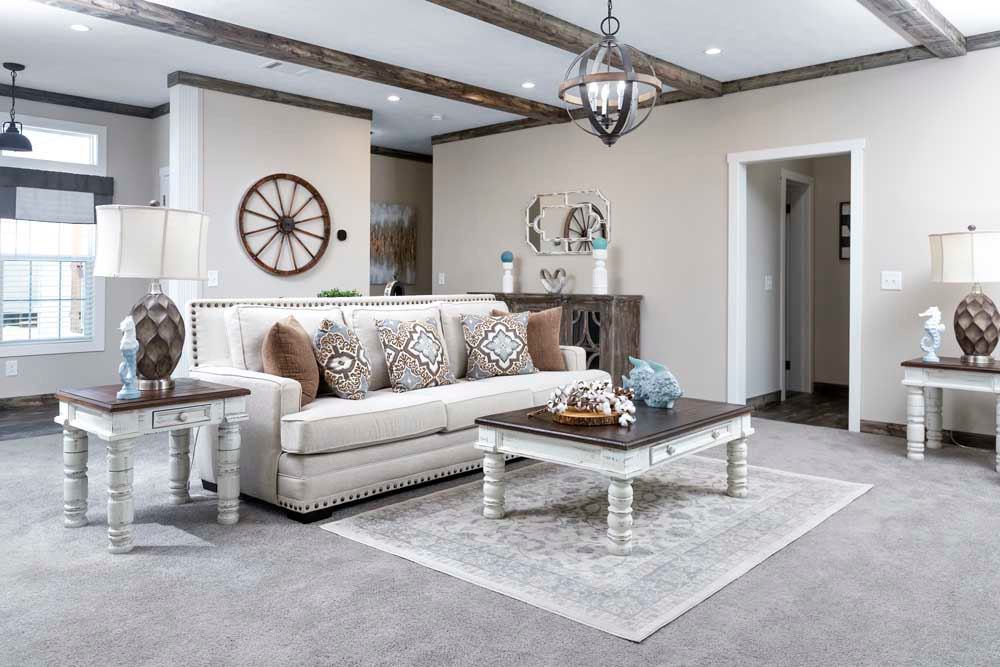 Stylish living room with beige sofa adorned with patterned pillows, rustic wooden beams, elegant lamps, and a coffee table on a patterned rug. Cozy and inviting.
