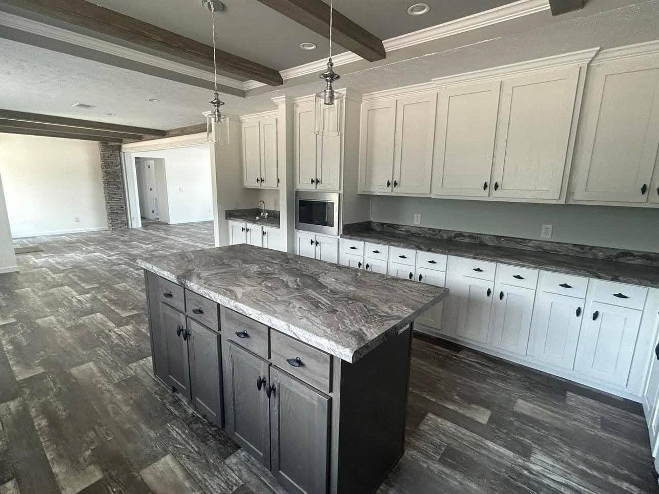 Modern kitchen with gray marble countertops, white cabinets, and dark wood island. Wood beams and pendant lights create a spacious, inviting atmosphere.