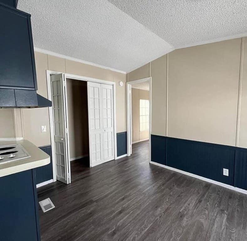 A modern room with dark wood floors, beige walls, and navy wainscoting. Sunlight filters through an open door, creating a bright, clean atmosphere.