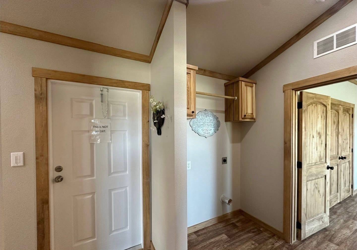 Compact entryway with wood accents, featuring a closed white door with a "This Is Not An Exit" sign. Corner shelf and hooks add subtle decoration.