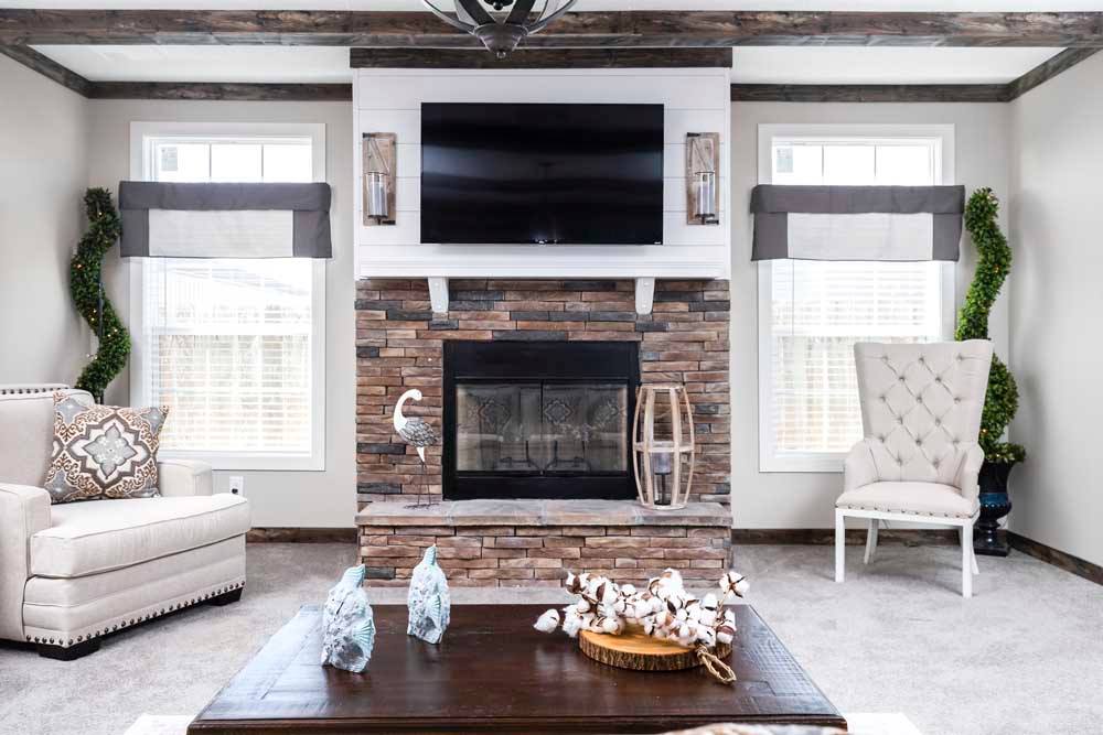 Cozy living room with a stone fireplace, wall-mounted TV, and elegant decor. Flanked by windows, an armchair, and sofa, it conveys warmth and comfort.