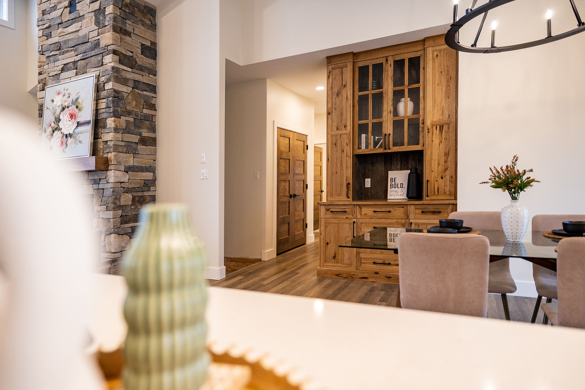 Cozy dining room with a stone fireplace, wooden cabinets, and a vase on a glass table. Warm lighting and modern decor create a welcoming ambiance.