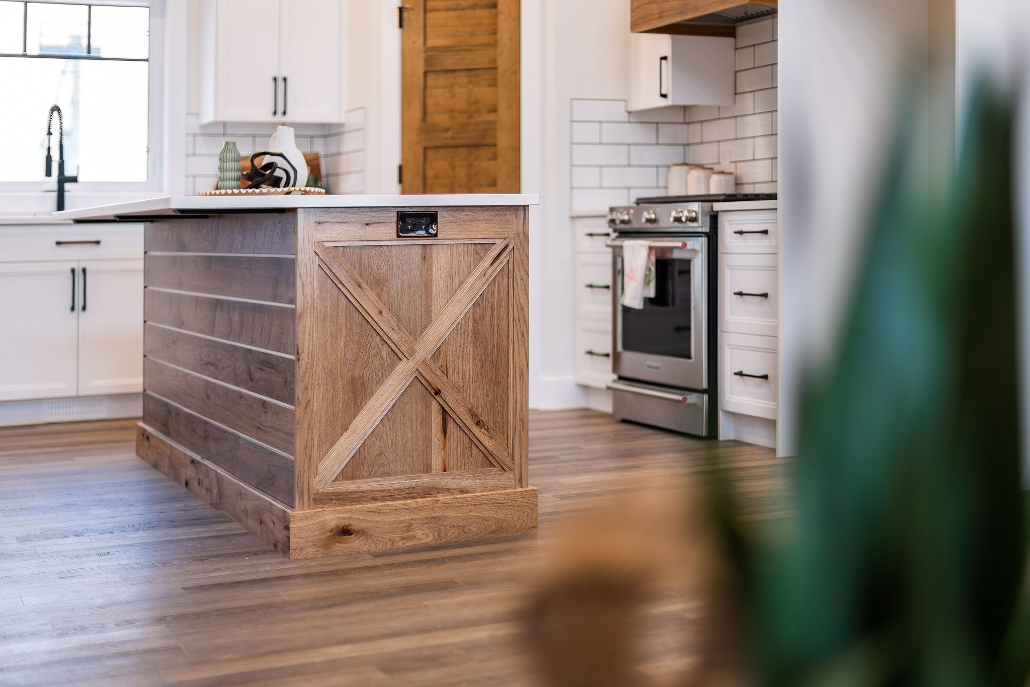 Modern kitchen with a rustic wooden island featuring an X-pattern design. White cabinets, stainless steel oven, and a tiled backsplash add a sleek contrast.