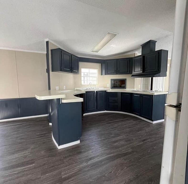 Modern kitchen with dark blue cabinets and white countertops. The room features dark wood floors, beige walls, and a window above the sink.