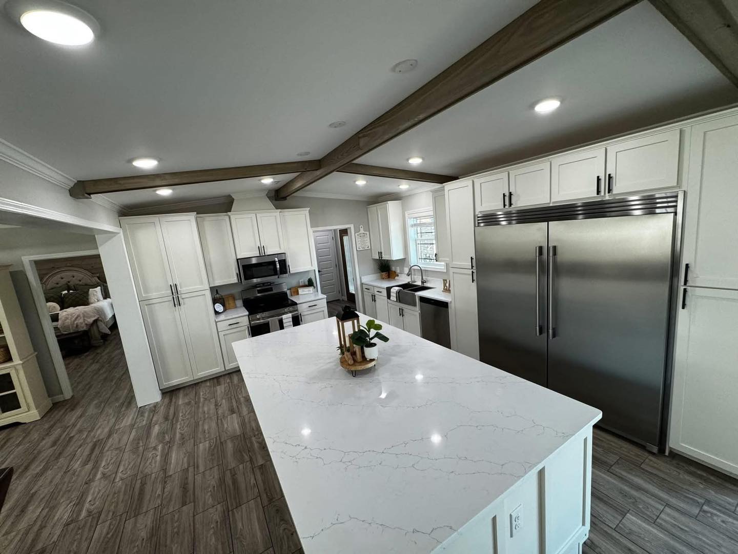Modern kitchen with white cabinetry, marble island, stainless steel appliances, and wood beam ceiling. Bright lighting creates a sleek, inviting atmosphere.