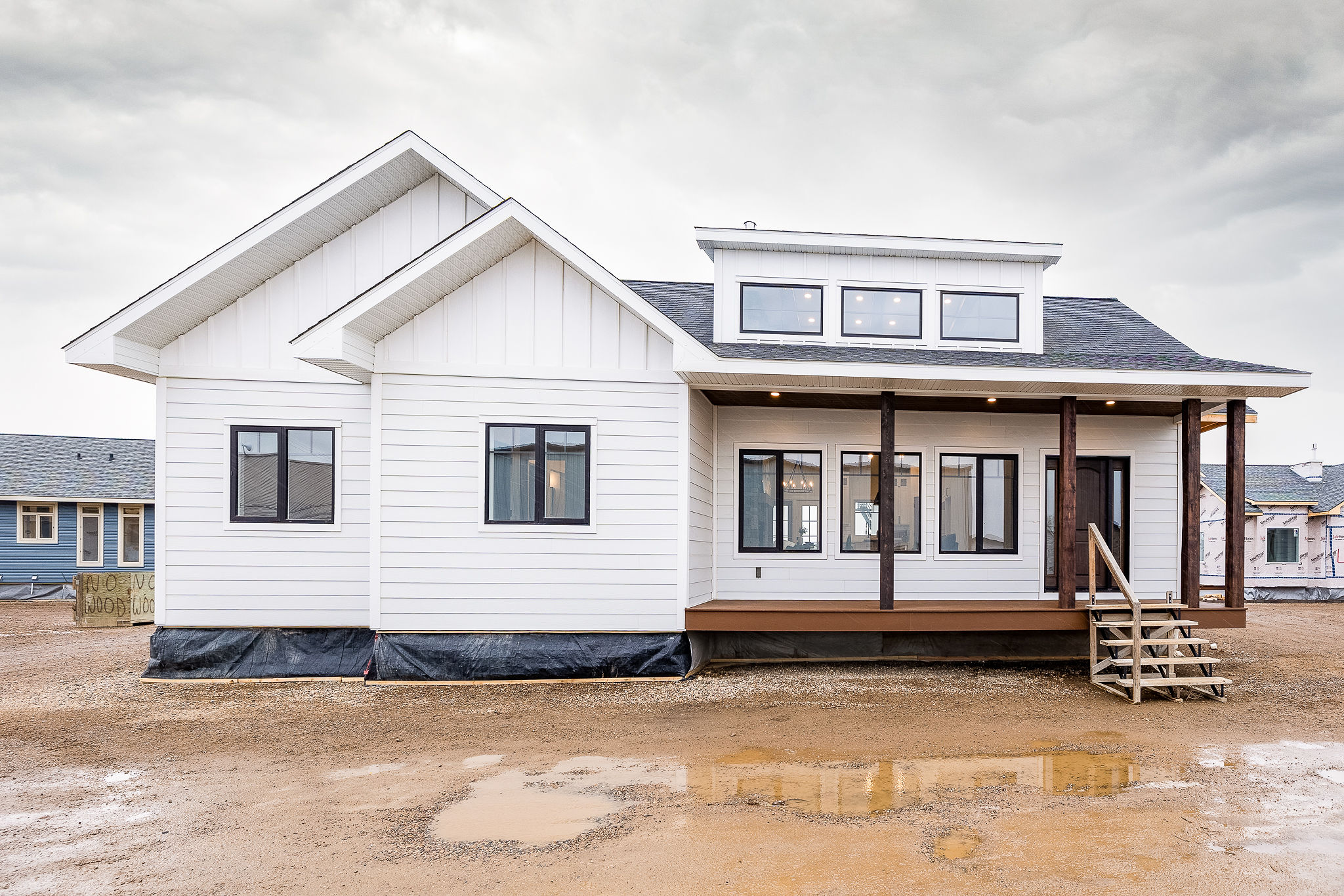 A modern, white modular home with large windows and a small wooden porch on a muddy construction site under a cloudy sky, conveying a fresh, new beginning.