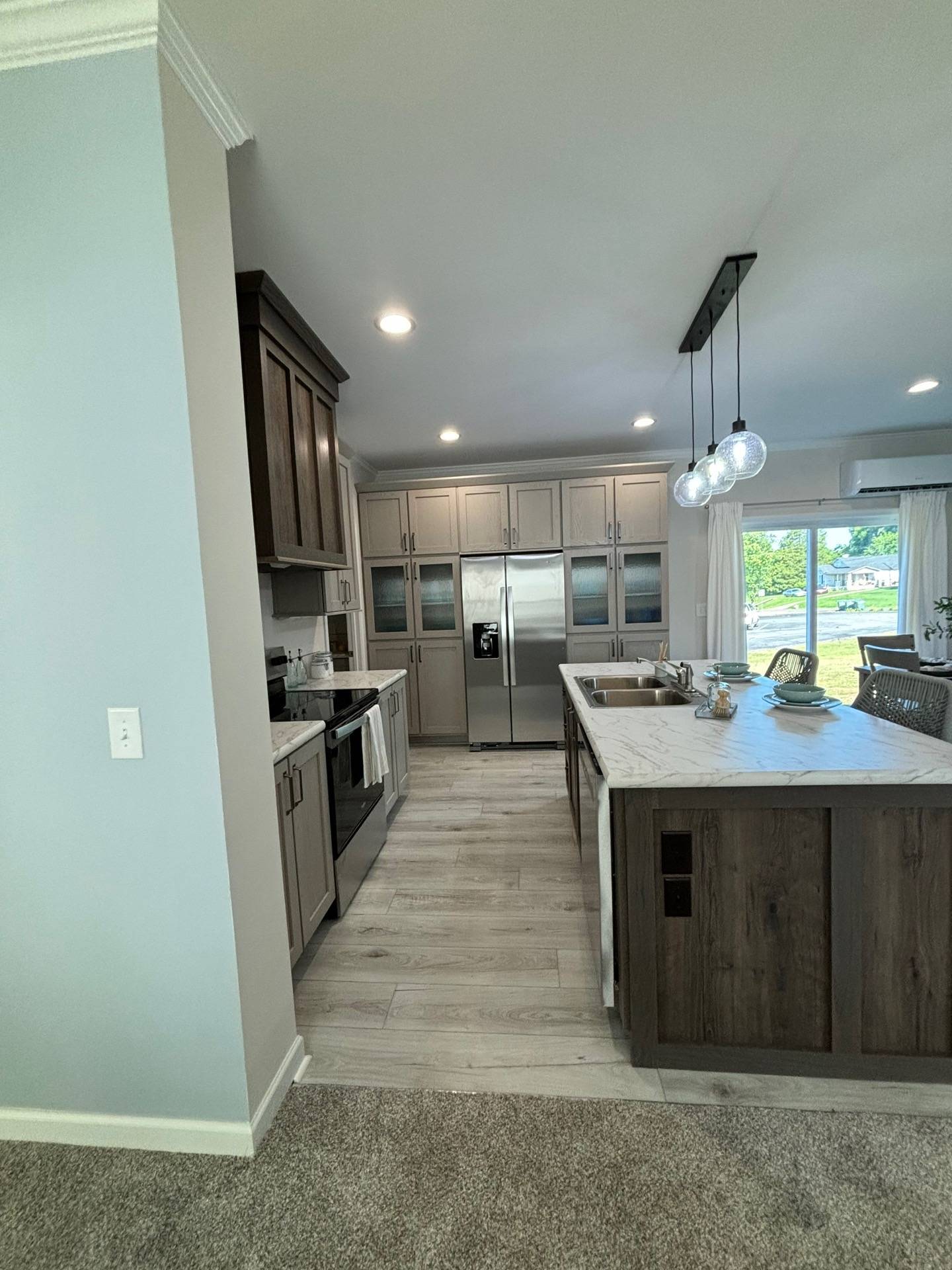 Modern kitchen with wood cabinets and stainless steel appliances. A marble island with pendant lights and table settings creates a welcoming atmosphere.