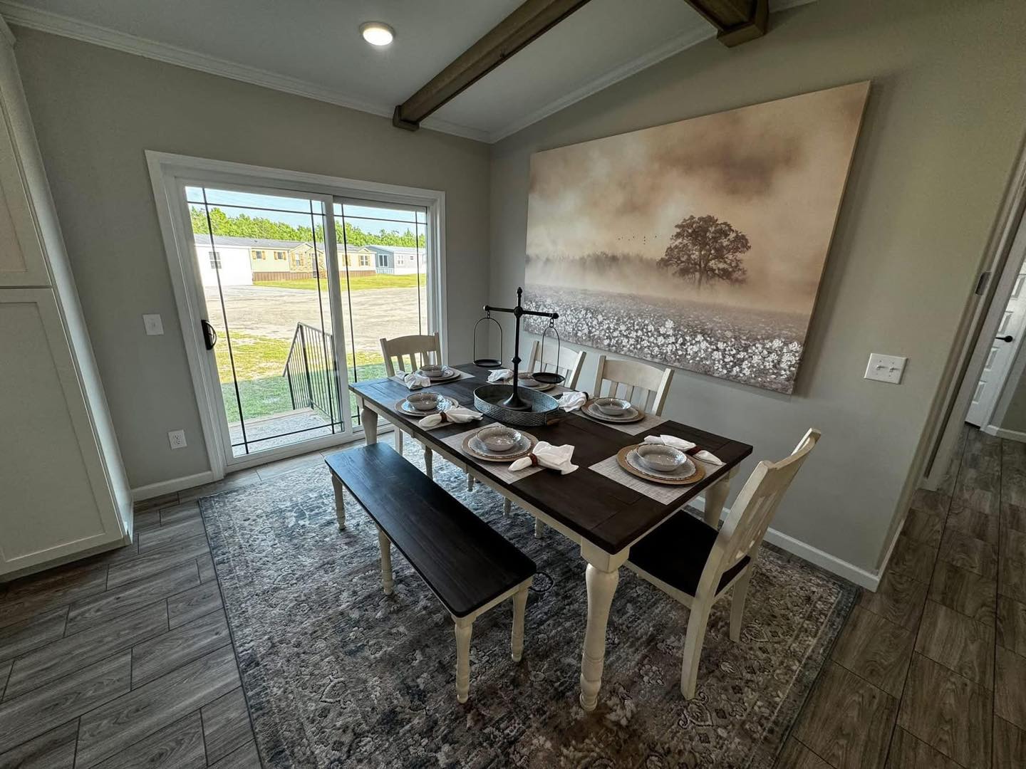 Cozy dining area with a wooden table set for six, featuring elegant dishware. A large, serene nature painting hangs on the wall, creating a calming ambiance.